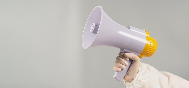 Hand houdt megafoon op grijze achtergrond Hand draagt een PBM-pak en een witte medische handschoen