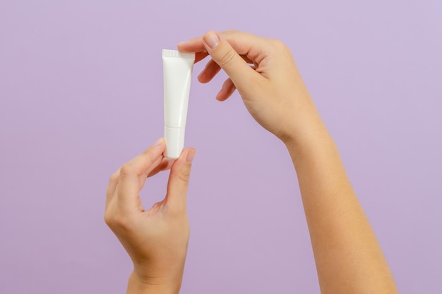 Hand houdt plastic witte buis geïsoleerd op lila achtergrond Schoonheidsconcept Verpakkingsbuis voor cosmetische producten