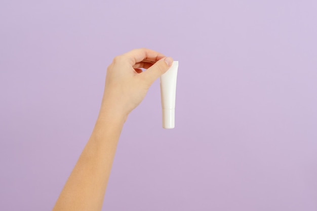 Hand houdt plastic witte buis geïsoleerd op lila achtergrond Schoonheidsconcept Verpakkingsbuis voor cosmetische producten