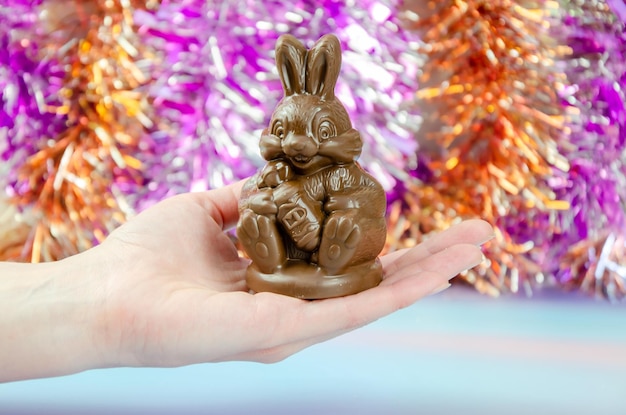 Hand houdt schattig chocoladekonijntje op glanzende achtergrond van veelkleurig klatergoud chocoladekonijntje in de hand