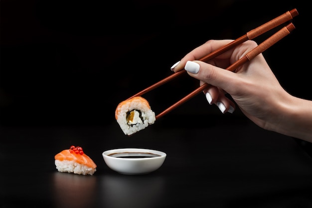 Hand houdt sushi boven kom met sojasaus op zwarte tafel.