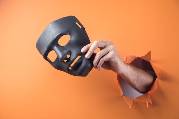 Hand houdt zwart masker op oranje achtergrond