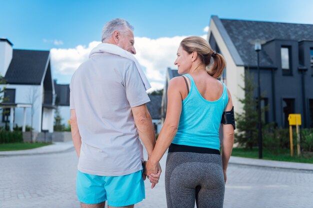 Hand of husband. Appealing blonde-haired woman holding hand of her handsome strong man while walking in the morning