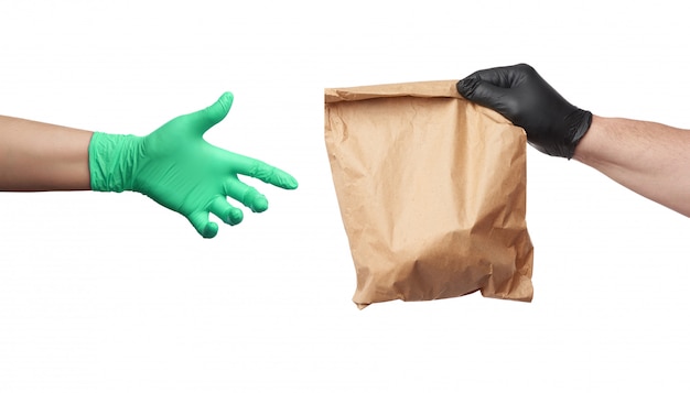 黒いラテックス手袋をはめた手は完全な茶色のパッケージを保持し、緑色の手袋をはめた女性の手は物体に手を伸ばします