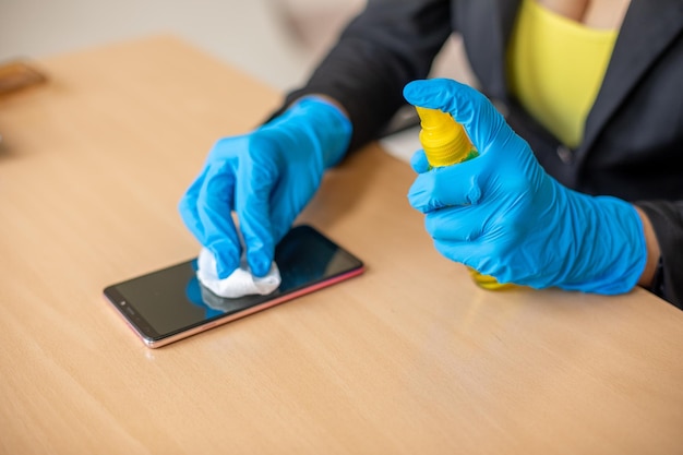 Hand in blauwe handschoenen ontsmettend schoonmaken smartphone mobiele telefoon op houten tafel met natte zakdoekjes