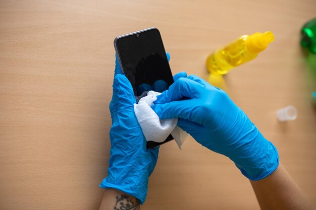 Фото Рука в голубых перчатках, дезинфекция, очистка смартфона, мобильный телефон на столе с мокрыми салфетками, алкоголь.