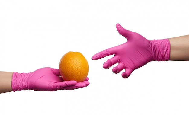 Hand in een roze latex handschoen houdt ronde rijp oranje