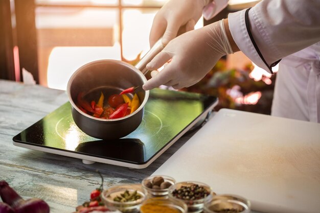 Hand in handschoen met steelpan plakjes kleurrijke groenten pittige pepers voor saus geheimen van cul...