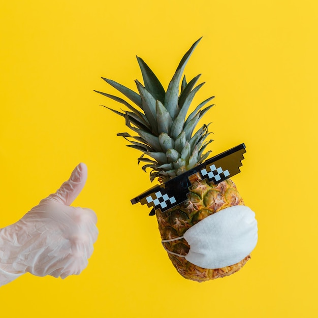 Foto hand in handschoen toont duim omhoog teken ananas fruit op zomer achtergrond concept tijdens coronavirus