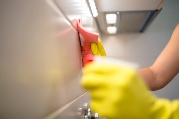 Hand in roze beschermende handschoen reinigen tegels met lap. Vroege lente schoonmaken of regelmatig opruimen. Reinigingsman reinigt huis.