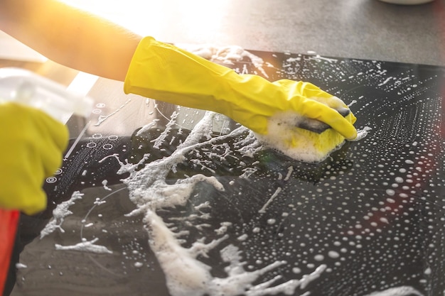 Hand in rubberen handschoen schoonmaken elektrisch fornuis met spuitfles en doek op een zonnige dag, keuken schoonmaak concept achtergrondfoto