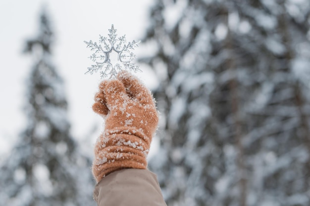 Hand in want met decoratieve transparante sneeuwvlok winter bos natuurlijke achtergrond