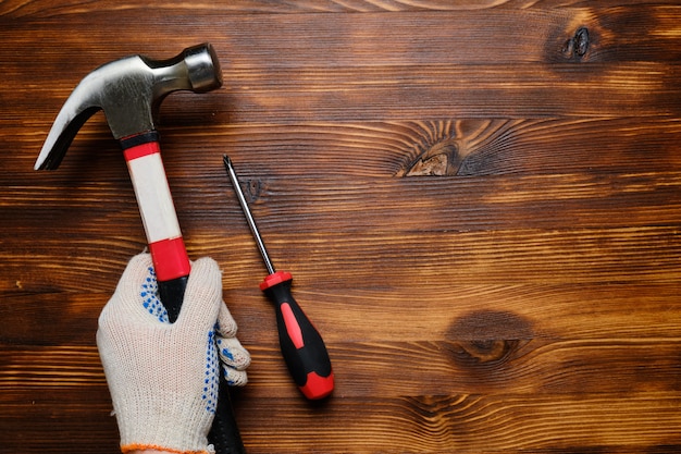 Hand in werkhandschoenen houdt hamer en schroevendraaier op houten muur met kopie ruimte.