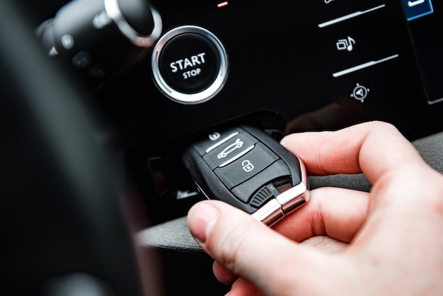 Hand insert car keyless remote in a keyhole in a car with start engine button.