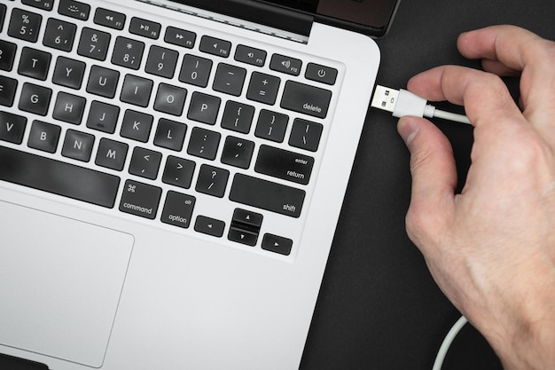 Hand insert usb wire in a gray laptop isolated on black Close up top view