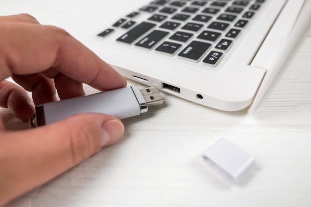 Hand inserting a USB flash drive into a laptop on a white background Closeup of woman's hand plug USB flash drive on laptop at home Copying data from a flash drive to a laptop