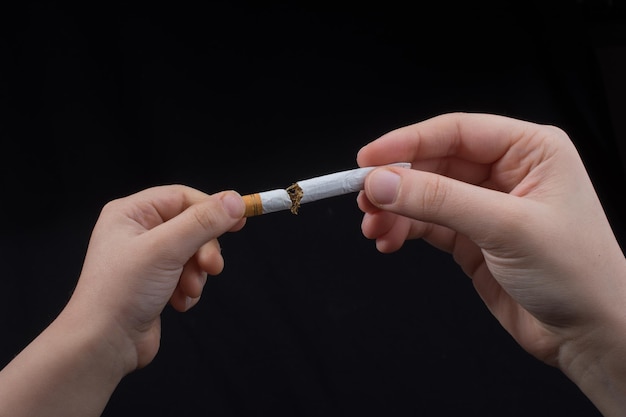 Hand is breaking a cigarette on black background