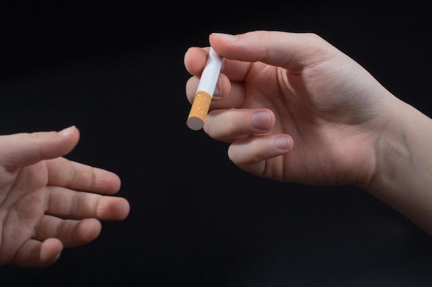 Hand is giving out cigarette on black background