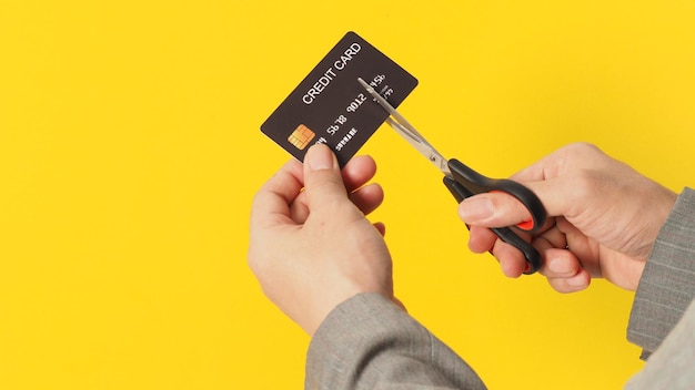 Hand is hold black credit card and scissors on yellow background Man arm wear a grey suit