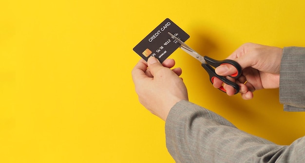 Hand is hold black credit card and scissors on yellow background Man arm wear a grey suit