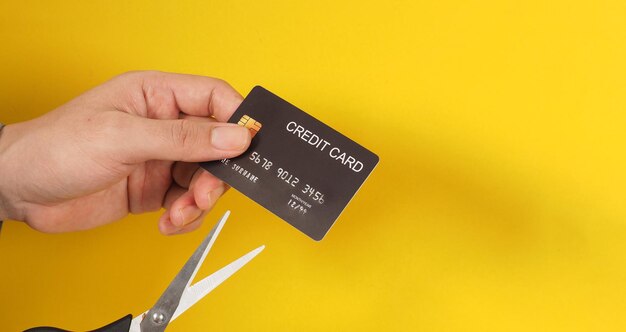 Hand is hold black credit card and scissors on yellow background