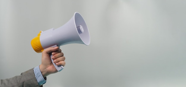 Hand is hold megaphone and wear grey suit on gray background.