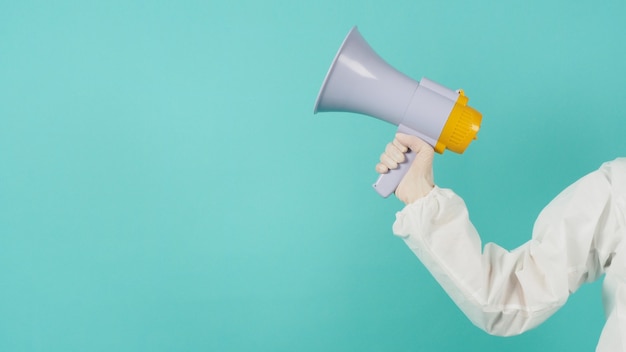 Hand is hold megaphone and wear PPE suit on green mint color or Tiffany Blue background.