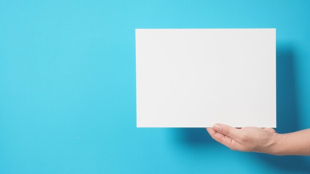 Hand is holding the A4 paper on blue background.