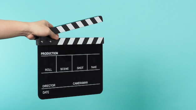 Photo hand is holding black clapper board or movie clapperboard or slate on green mint or tiffany blue background.