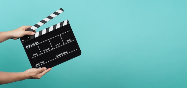 Hand is holding Black clapper board or movie slate on blue and green or Turquoise background.