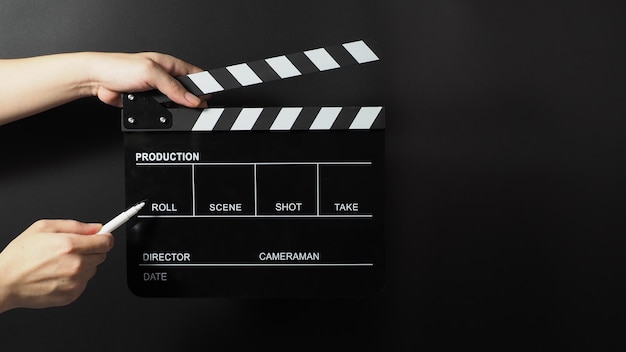 Hand is holding black clapper board or movie slate and marker Pen on black background