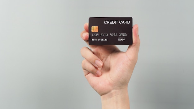 hand is holding black credit card isolated on grey background.