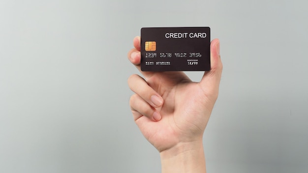 Hand is holding black credit card isolated on grey background.