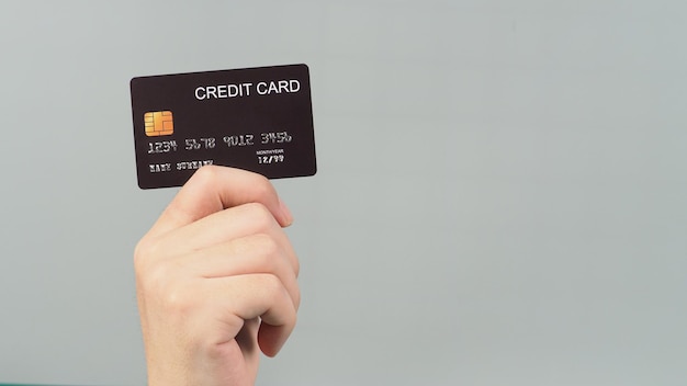 Рука держит черную кредитную карту, изолированную на сером фоне.