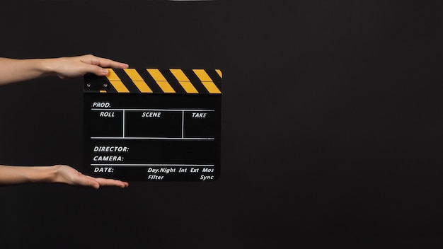 手は、黒い背景に黄色のカチンコまたはビデオ制作や映画産業で使用される映画のスレートで黒を保持しています。