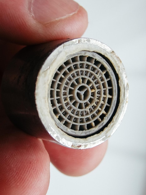 Photo hand is holding a chrome faucet aerator covered with lime scale faucet contaminated with calcium limescale on tap mixer