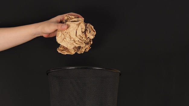 The hand is holding a crumpled brown paper maul and trash can on black background