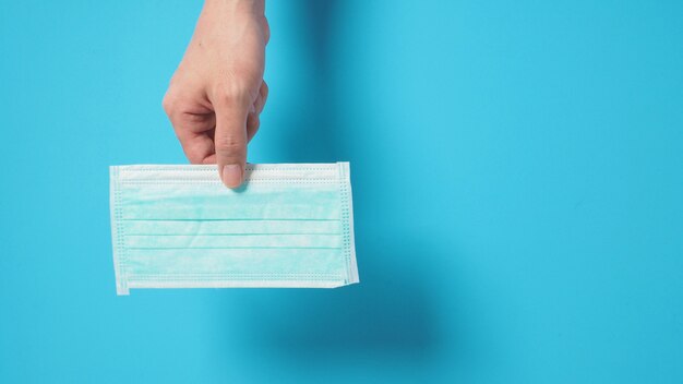 Hand is holding face Mask for protection from virus infection and chemical. Put on blue background.