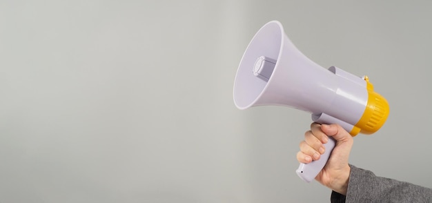 A hand is holding megaphone and  wearing a dark grey Tshirt on grey background