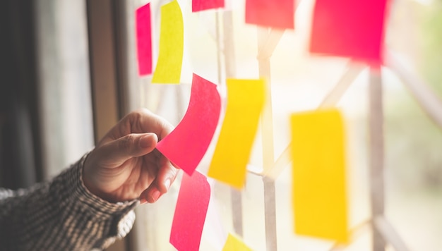 Hand is holding the post it notes attached to the glass wall. Concept brainstorming, share idea.