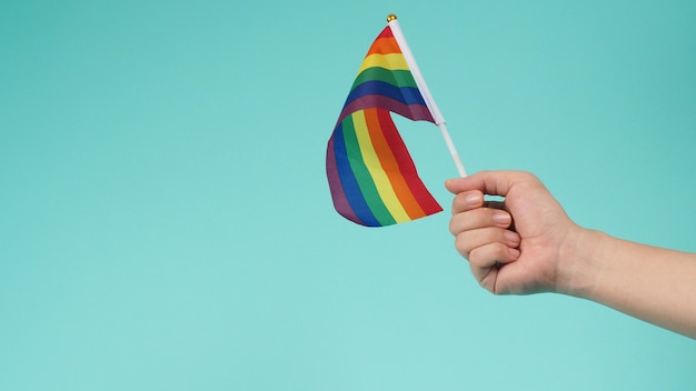 La mano tiene una bandiera arcobaleno su sfondo verde menta o blu tiffany.