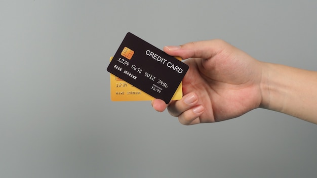 La mano tiene due carte di credito in colore nero e oro isolate su sfondo grigio.