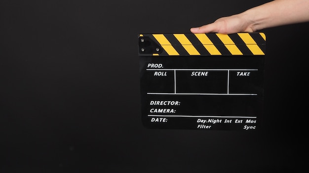 Hand is holding yellow and black color movie slate.It is used in video production and film industry on black background.