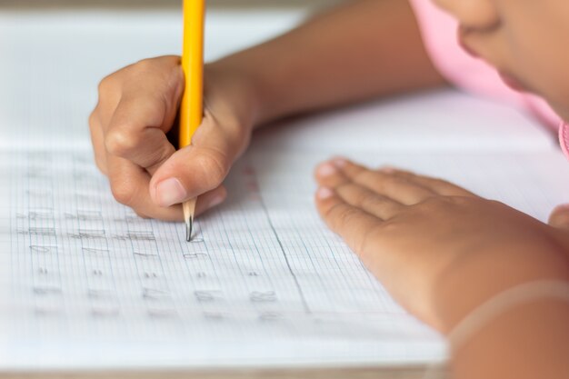 Photo hand is holding a yellow pencil and writing in a notebook