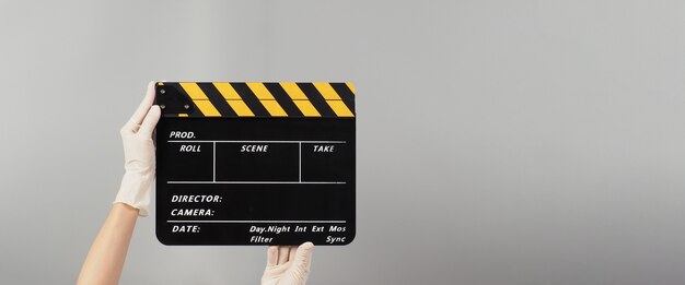 Hand is holding yellow with black clapper board color and wear white medical glove.It is used in video production and film industry on grey background.