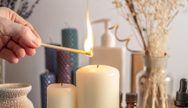 Hand is lighting the candle with a burning match There is aroma lamp candles and cosmetics on the table Concept of aromatherapy relaxing atmosphere