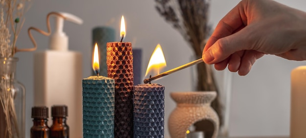 Hand is lighting the candle with a burning match There is aroma lamp candles and cosmetics on the table Concept of aromatherapy relaxing atmosphere