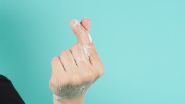 Photo hand is do a mini heart hand sign and have foam soap bubbles on a green mint background.isolated