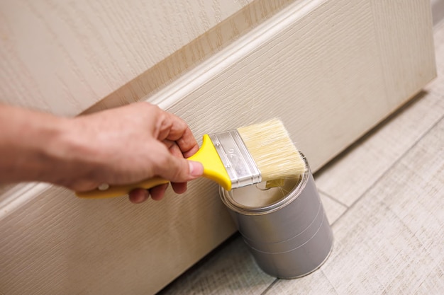 Close-up of a hand holding a paint brush, illustrating door painting and repair work.