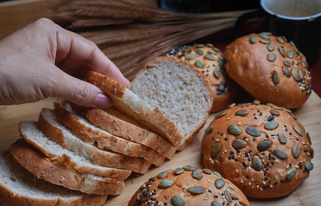 A hand is picking up a slice of bread from a wooden tray.